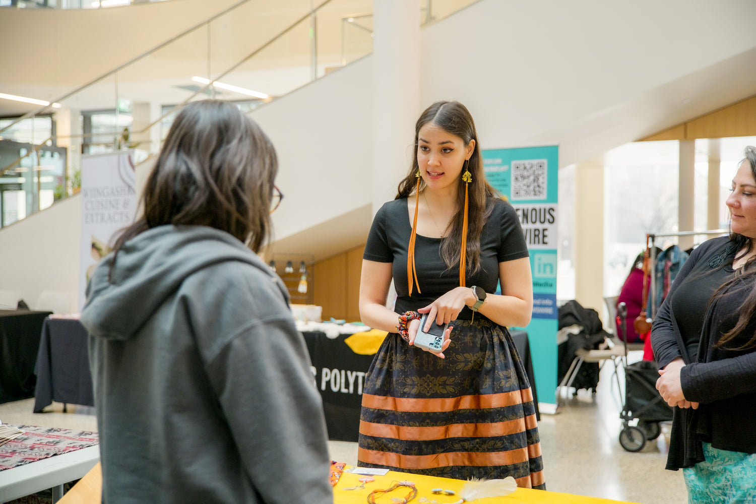 Woman in a black and orange dress standing at a booth with other people.