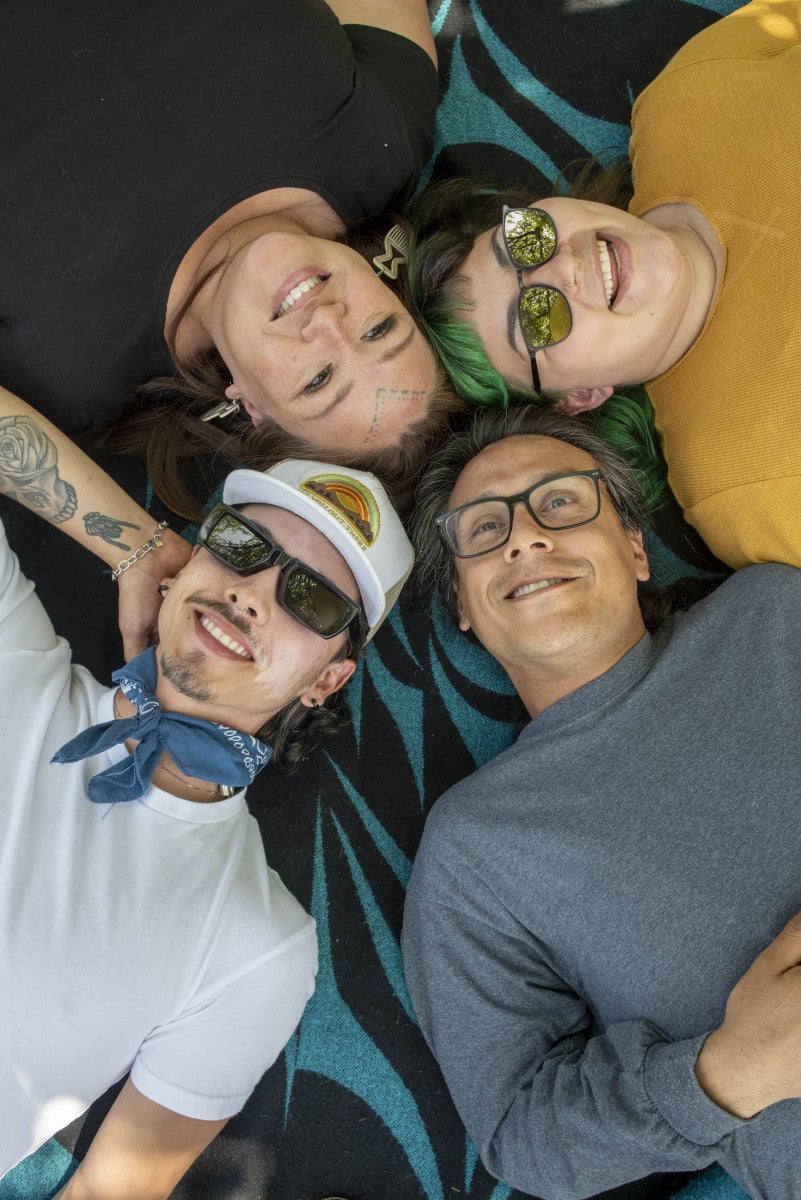 Four people lying on a colorful blanket, smiling and posing for a selfie.